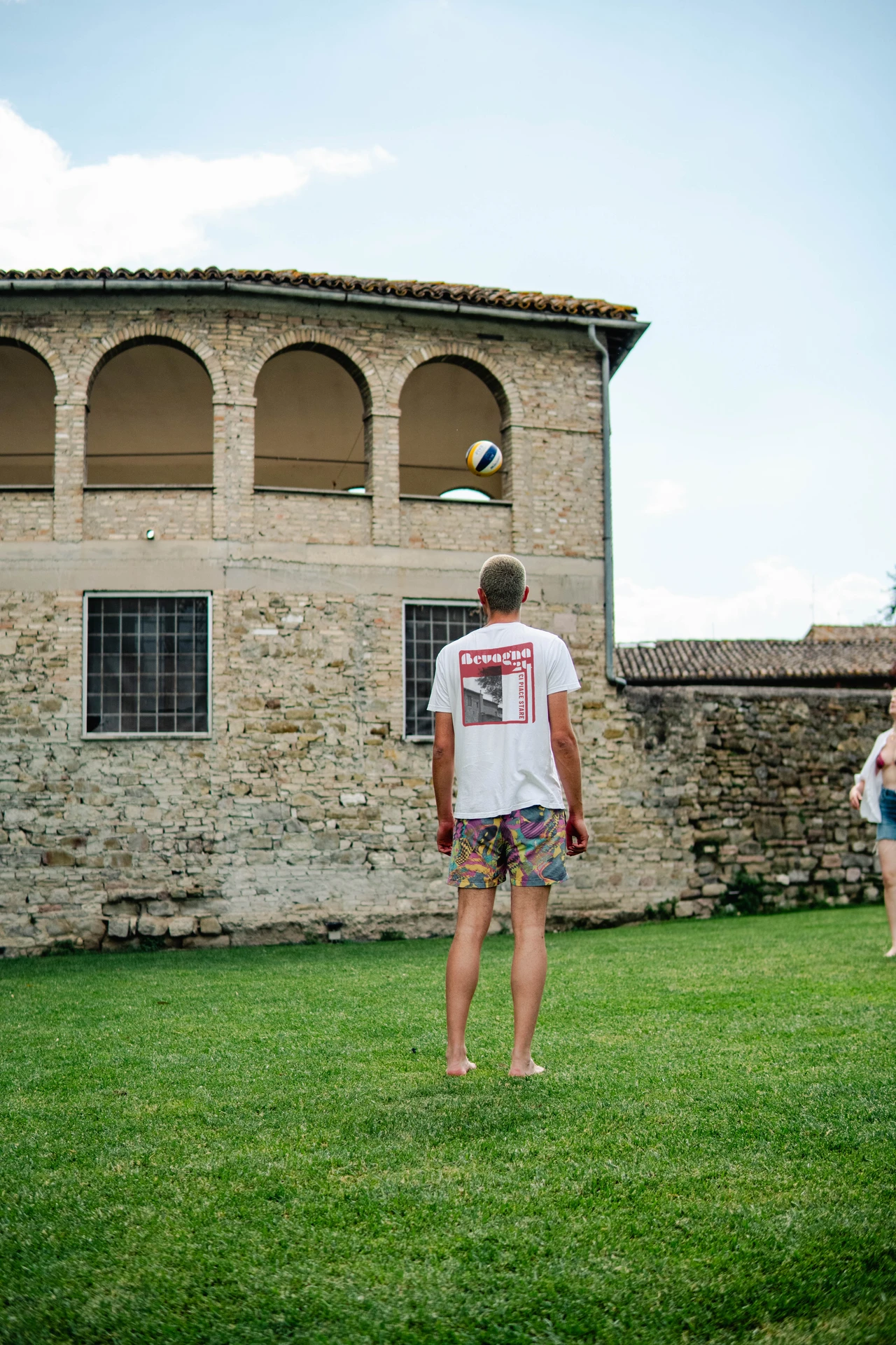 Raphael trägt bedrucktes T-Shirt auf einer Wiese vor historischer Architektur in Bevagna