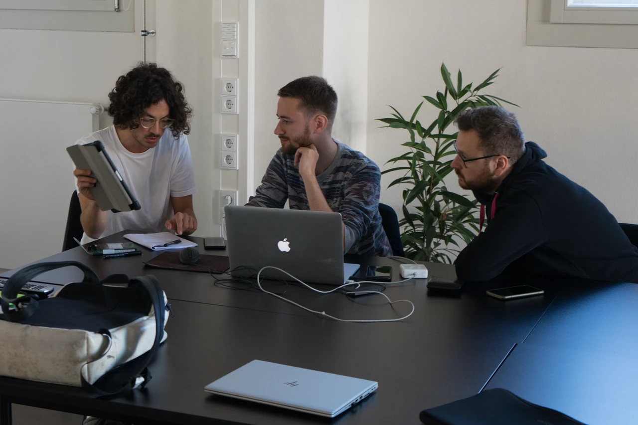 Raphael und zwei weitere Teammitglieder arbeiten gemeinsam an Konzept und Interface mit Laptop und Tablet
